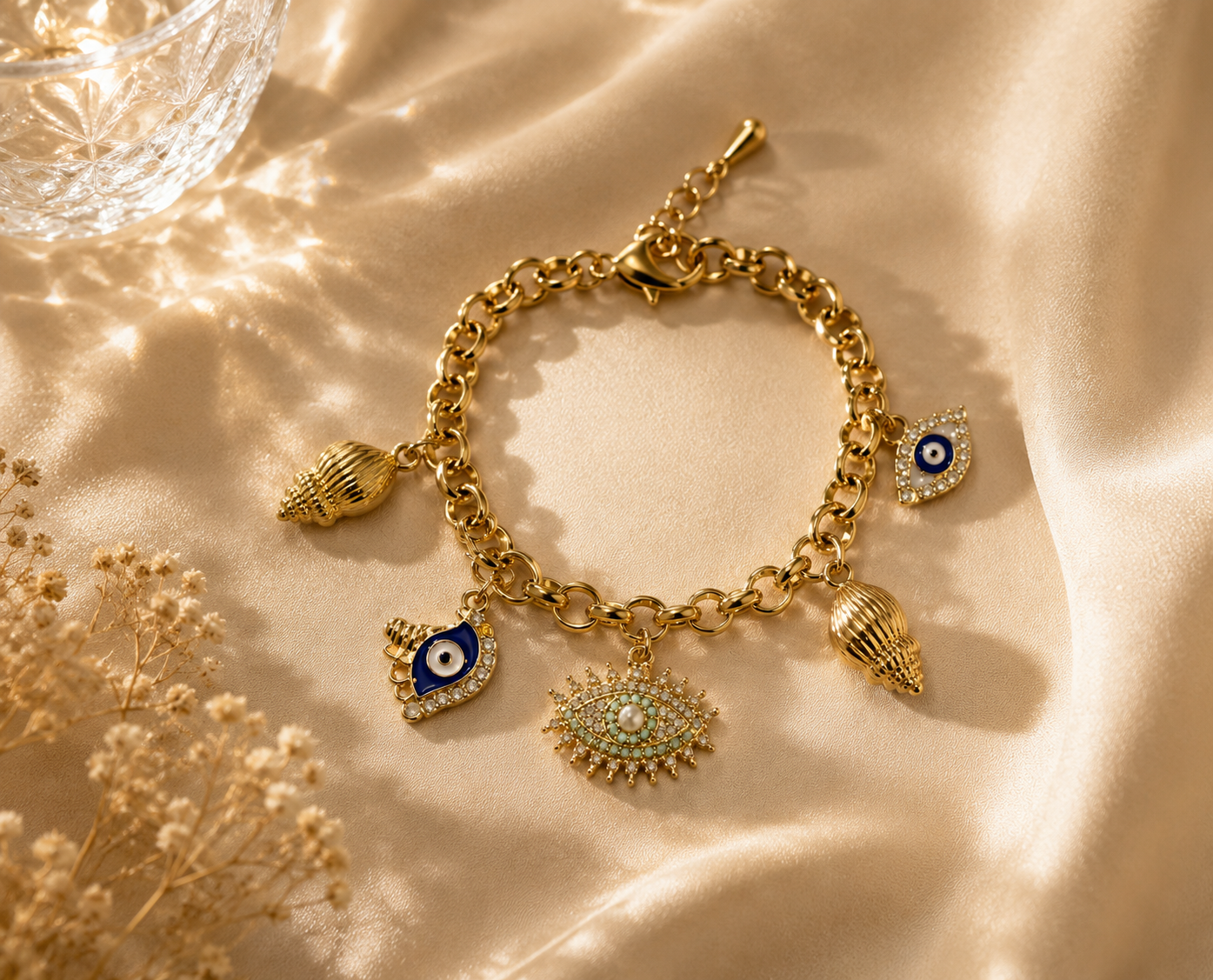 Vrenora gold charm bracelet featuring evil eye, shell, and turquoise eye charms displayed on luxurious champagne satin fabric.