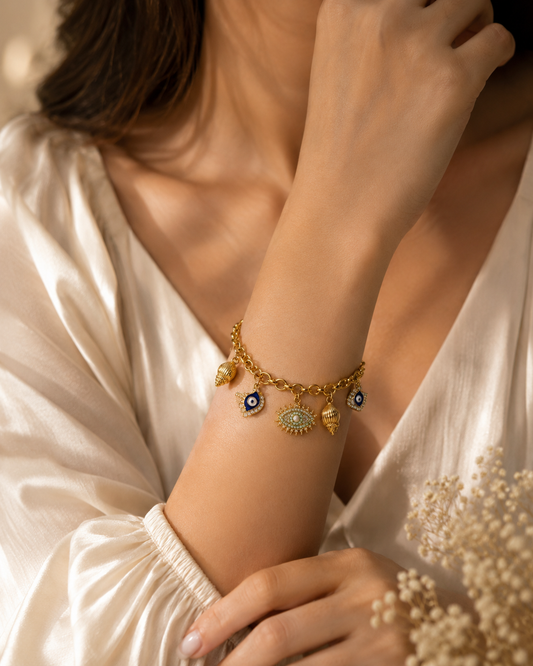 Model wearing the Vrenora Evil Eye Gold Charm Bracelet featuring blue evil eye, shell, and turquoise charms with a luxurious gold-plated finish.